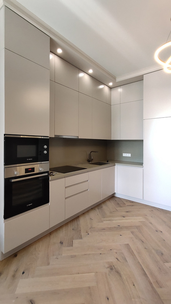 This is an example of a contemporary l-shaped kitchen in Moscow with an undermount sink, flat-panel cabinets, grey splashback, stainless steel appliances, beige floor and grey benchtop.