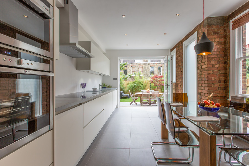 This is an example of a contemporary single-wall eat-in kitchen in London with an undermount sink, flat-panel cabinets, white cabinets, stainless steel appliances and no island.
