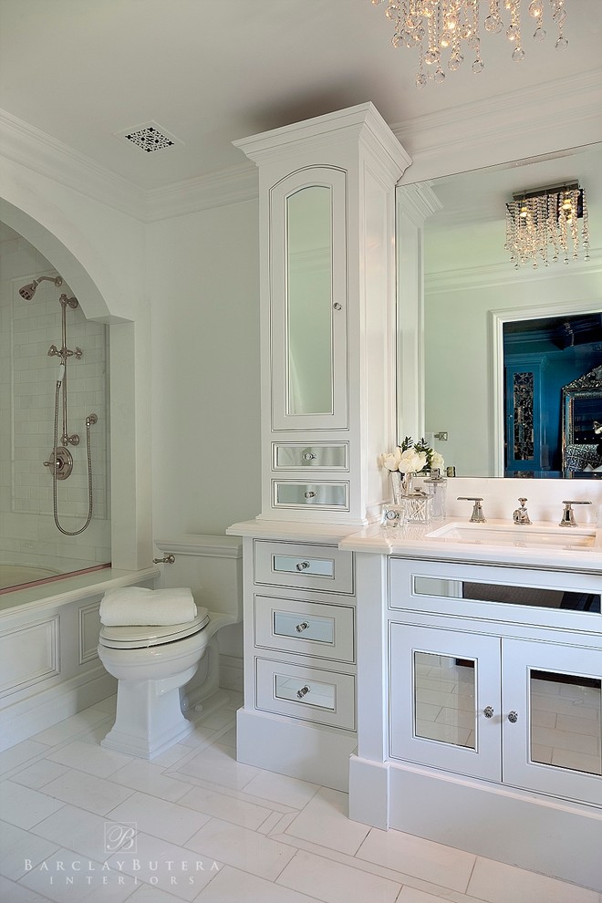 This is an example of an eclectic master bathroom in Orange County with an undermount sink, furniture-like cabinets, white cabinets, engineered quartz benchtops, an alcove tub, a shower/bathtub combo, a one-piece toilet, white tile, subway tile, white walls and marble floors.