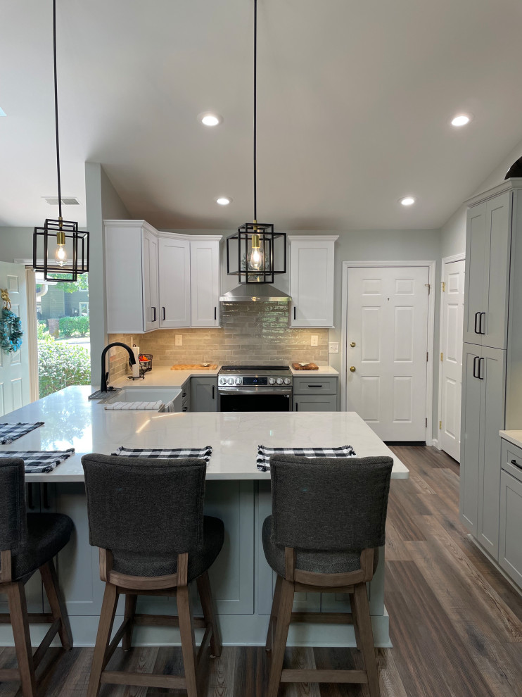 Example of a mid-sized transitional u-shaped vinyl floor and brown floor eat-in kitchen design with a farmhouse sink, shaker cabinets, white cabinets, quartz countertops, gray backsplash, subway tile backsplash, stainless steel appliances, no island and white countertops
