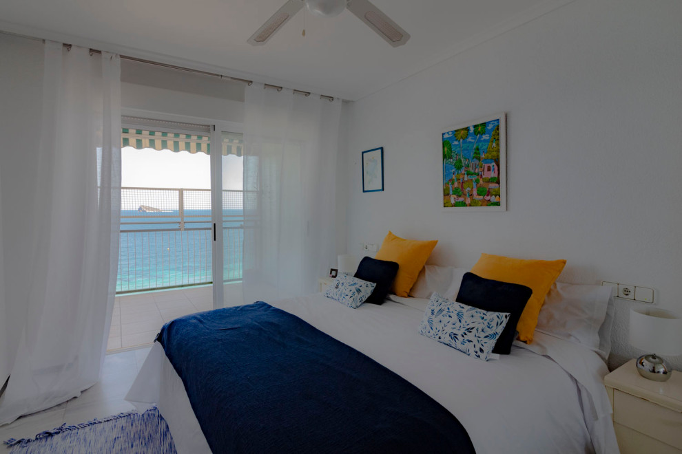 Ejemplo de dormitorio principal costero con paredes blancas, suelo de mármol y suelo blanco