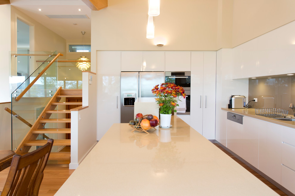 This is an example of a contemporary kitchen in Sydney with an undermount sink, quartz benchtops, glass sheet splashback, stainless steel appliances, light hardwood floors and with island.