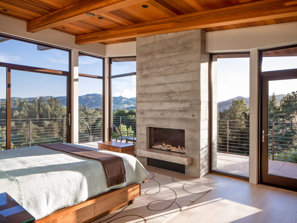 Photo of a large contemporary master bedroom in San Francisco with white walls, light hardwood floors, a standard fireplace, a concrete fireplace surround and white floor.
