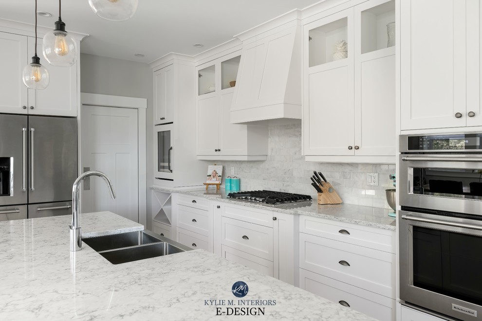Mid-sized transitional l-shaped open plan kitchen in Vancouver with a farmhouse sink, shaker cabinets, white cabinets, quartz benchtops, multi-coloured splashback, marble splashback, stainless steel appliances, medium hardwood floors, with island and white benchtop.