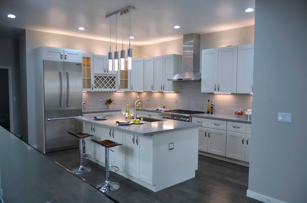 This is an example of a modern eat-in kitchen in Sacramento with a single-bowl sink, flat-panel cabinets, white cabinets, limestone benchtops, white splashback, ceramic splashback, stainless steel appliances, medium hardwood floors and with island.