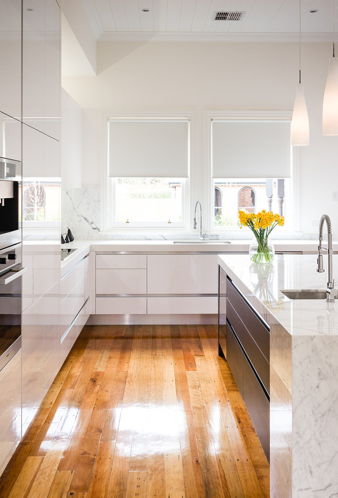 Inspiration for an expansive modern l-shaped eat-in kitchen in Melbourne with an undermount sink, flat-panel cabinets, white cabinets, marble benchtops, stone slab splashback, light hardwood floors, with island and stainless steel appliances.