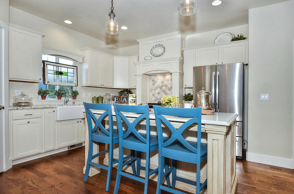 Mid-sized arts and crafts u-shaped kitchen in Denver with a farmhouse sink, shaker cabinets, white cabinets, quartz benchtops, white splashback, ceramic splashback, stainless steel appliances, medium hardwood floors, with island, brown floor and multi-coloured benchtop.