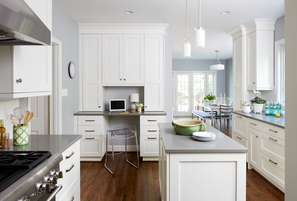 Example of a mid-sized transitional u-shaped dark wood floor and brown floor enclosed kitchen design in DC Metro with a farmhouse sink, shaker cabinets, white cabinets, solid surface countertops, white backsplash, subway tile backsplash, stainless steel appliances and an island