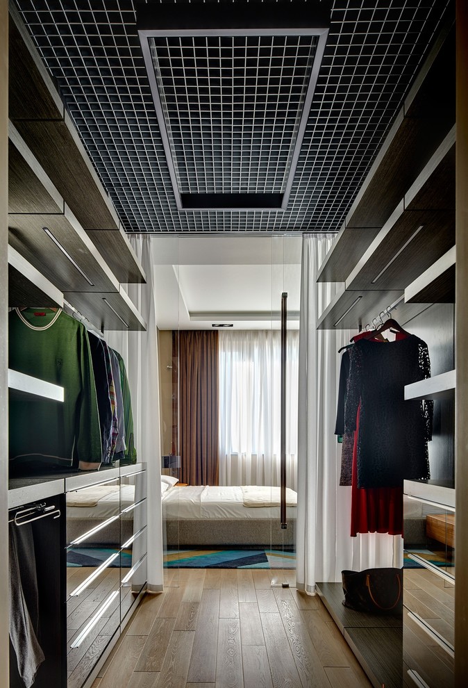 This is an example of a contemporary gender-neutral walk-in wardrobe in Moscow with flat-panel cabinets, medium hardwood floors and brown floor.