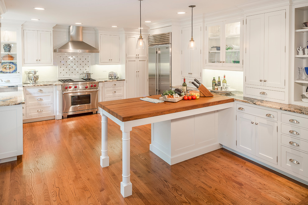 Photo of a traditional u-shaped kitchen in Chicago with shaker cabinets, white cabinets, white splashback, stainless steel appliances, medium hardwood floors, a peninsula and brown floor.