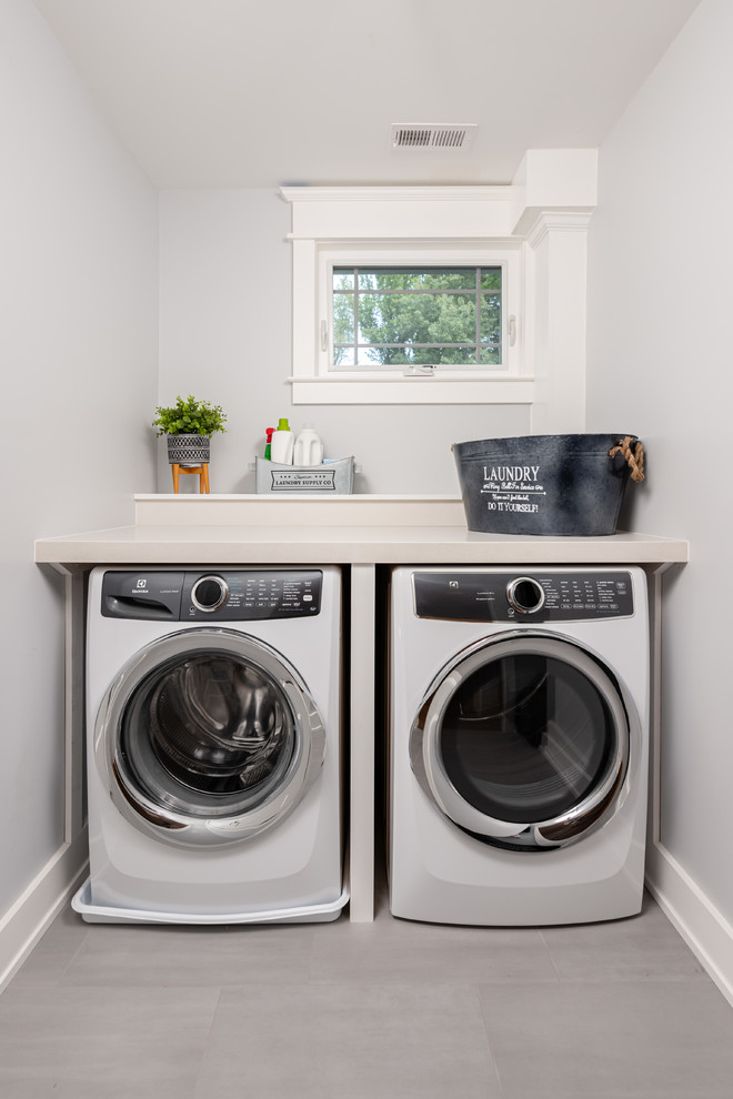 Mid-sized transitional single-wall dedicated laundry room in DC Metro with grey walls, a side-by-side washer and dryer, grey floor, solid surface benchtops and beige benchtop.