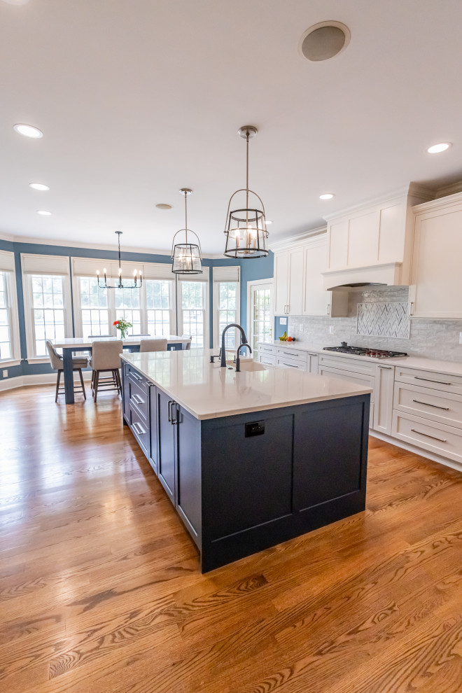 Inspiration for a large transitional u-shaped medium tone wood floor and brown floor eat-in kitchen remodel in Baltimore with a farmhouse sink, shaker cabinets, blue cabinets, quartz countertops, white backsplash, marble backsplash, stainless steel appliances, an island and white countertops