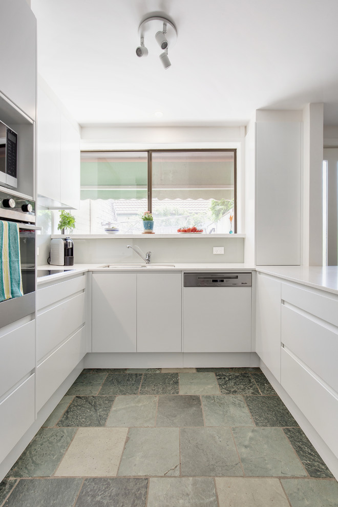 Design ideas for a contemporary u-shaped kitchen in Sydney with an undermount sink, flat-panel cabinets, white cabinets, white splashback, stainless steel appliances, a peninsula, blue floor and white benchtop.