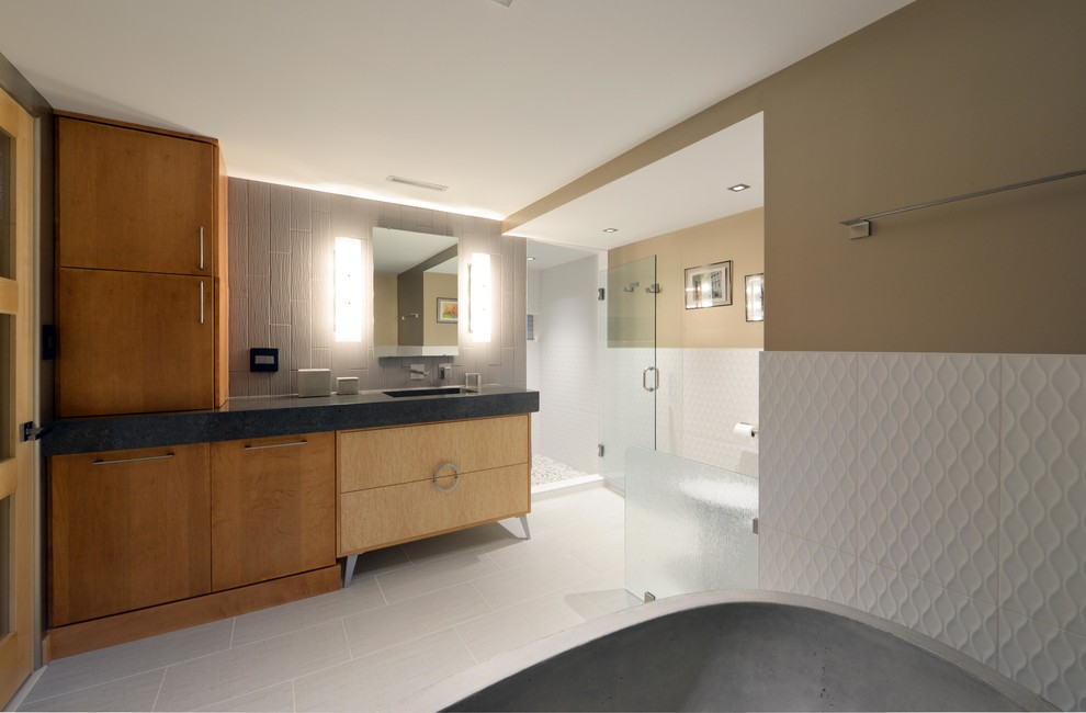 Photo of a small midcentury master bathroom in Other with flat-panel cabinets, light wood cabinets, a freestanding tub, an alcove shower, a one-piece toilet, gray tile, porcelain tile, grey walls, porcelain floors, an integrated sink, quartzite benchtops, grey floor, a hinged shower door and black benchtops.