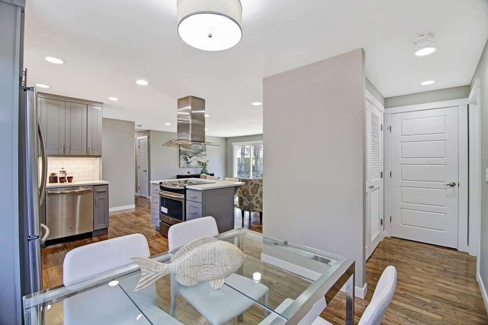 Inspiration for a mid-sized transitional l-shaped medium tone wood floor and brown floor eat-in kitchen remodel in Seattle with an undermount sink, shaker cabinets, gray cabinets, quartz countertops, white backsplash, ceramic backsplash, stainless steel appliances, an island and white countertops