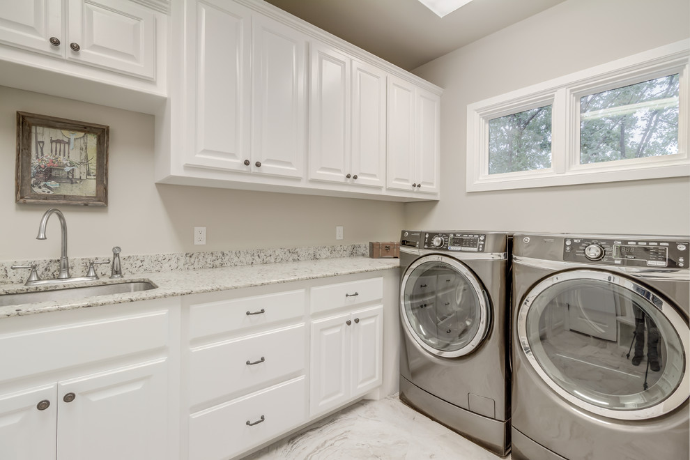 Mid-sized country l-shaped dedicated laundry room in Oklahoma City with an undermount sink, raised-panel cabinets, white cabinets, quartz benchtops, grey walls, ceramic floors, a side-by-side washer and dryer and grey floor.