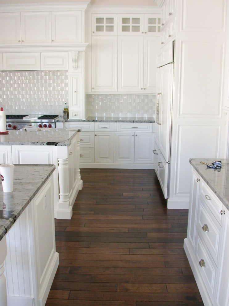 Inspiration for a large transitional dark wood floor and brown floor kitchen remodel in Phoenix with raised-panel cabinets, white cabinets, granite countertops, white backsplash, stainless steel appliances and two islands