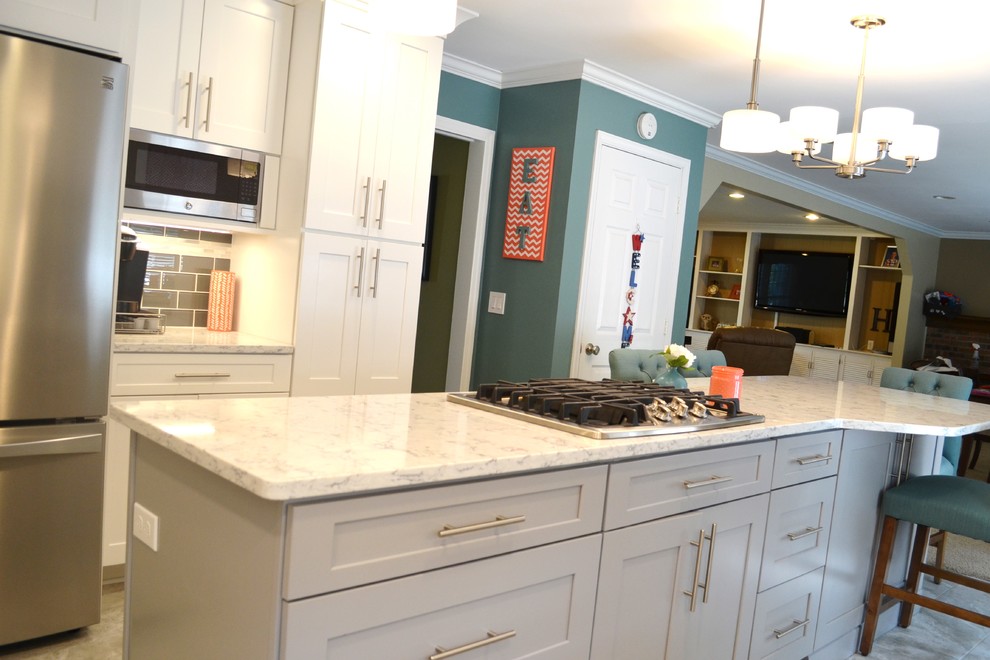 Photo of a mid-sized transitional u-shaped eat-in kitchen in Grand Rapids with a farmhouse sink, shaker cabinets, white cabinets, quartz benchtops, grey splashback, subway tile splashback, stainless steel appliances, ceramic floors and with island.