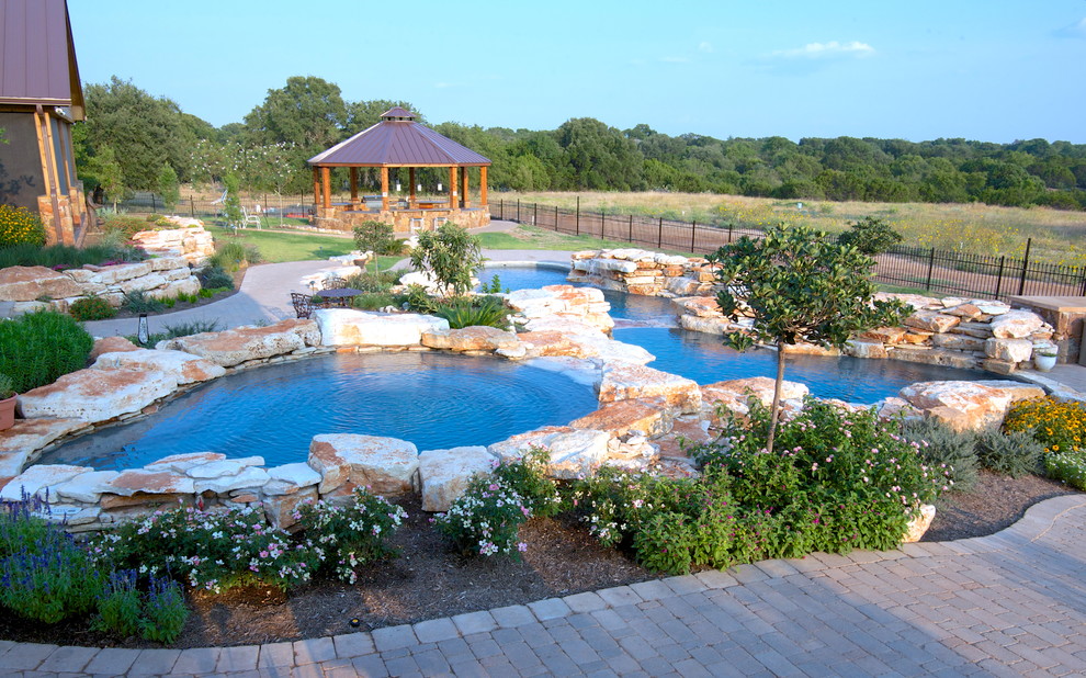 Photo of an expansive country backyard custom-shaped natural pool in Dallas with a water feature and natural stone pavers.