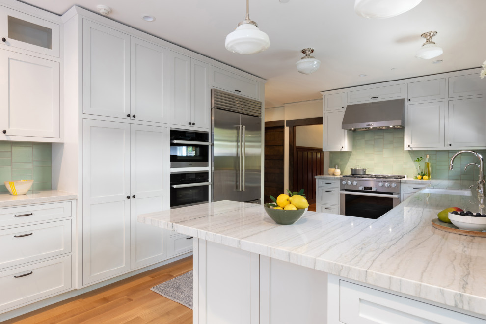 Photo of a large arts and crafts u-shaped kitchen in Los Angeles with a farmhouse sink, shaker cabinets, grey cabinets, quartzite benchtops, green splashback, ceramic splashback, stainless steel appliances, light hardwood floors, a peninsula and grey benchtop.