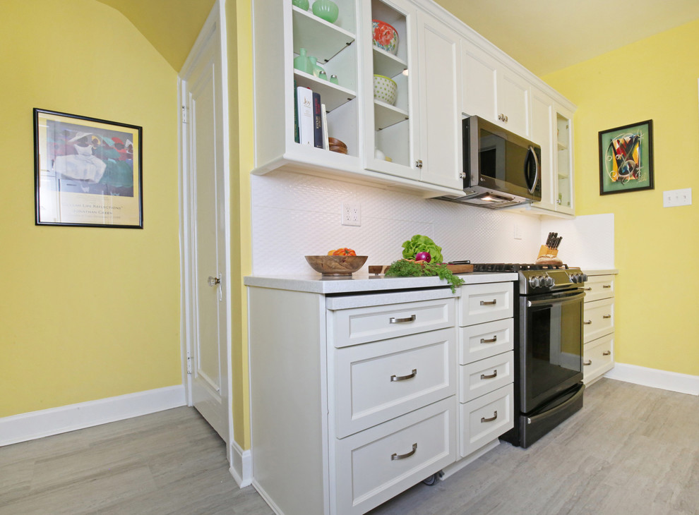 This is an example of a small transitional galley separate kitchen in Louisville with a double-bowl sink, recessed-panel cabinets, white cabinets, solid surface benchtops, white splashback, ceramic splashback, stainless steel appliances, vinyl floors, no island, grey floor and white benchtop.