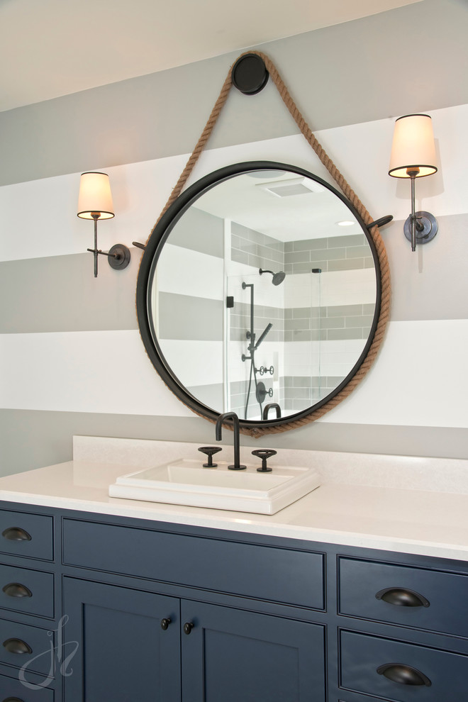 Inspiration for a mid-sized transitional kids bathroom in Detroit with beaded inset cabinets, blue cabinets, a one-piece toilet, white tile, subway tile, grey walls, marble floors, quartzite benchtops, an alcove tub, a shower/bathtub combo, a drop-in sink, a hinged shower door and white floor.