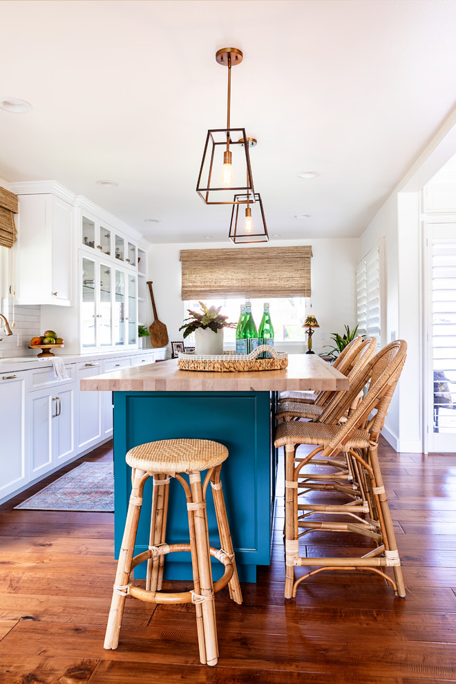 Expansive beach style galley eat-in kitchen in Los Angeles with a farmhouse sink, shaker cabinets, white cabinets, quartzite benchtops, white splashback, subway tile splashback, panelled appliances, medium hardwood floors, with island, brown floor and white benchtop.