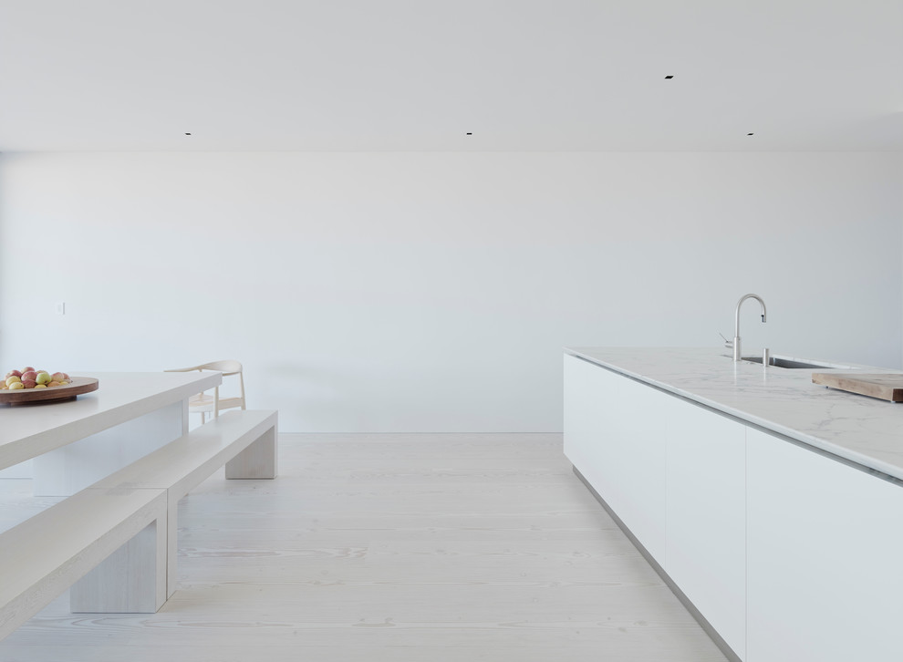 Inspiration for a mid-sized contemporary l-shaped eat-in kitchen in San Francisco with a single-bowl sink, flat-panel cabinets, white cabinets, marble benchtops, white splashback, white appliances, light hardwood floors and with island.