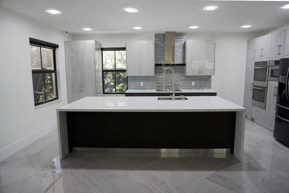 Large modern l-shaped eat-in kitchen in Miami with an undermount sink, flat-panel cabinets, grey cabinets, quartz benchtops, grey splashback, glass tile splashback, stainless steel appliances, porcelain floors, with island, grey floor and white benchtop.