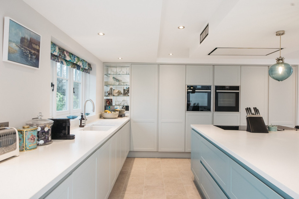 This is an example of a contemporary eat-in kitchen in Buckinghamshire with blue cabinets, black appliances, with island and white benchtop.