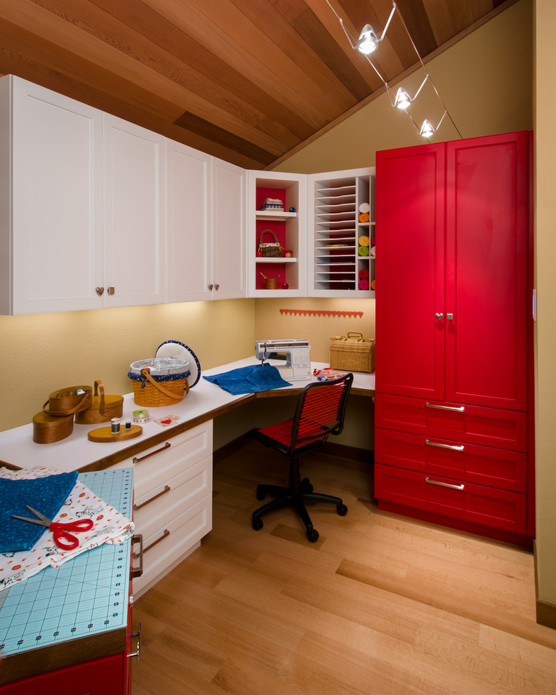This is an example of a craft room in San Francisco with yellow walls, medium hardwood floors, a built-in desk and black floor.