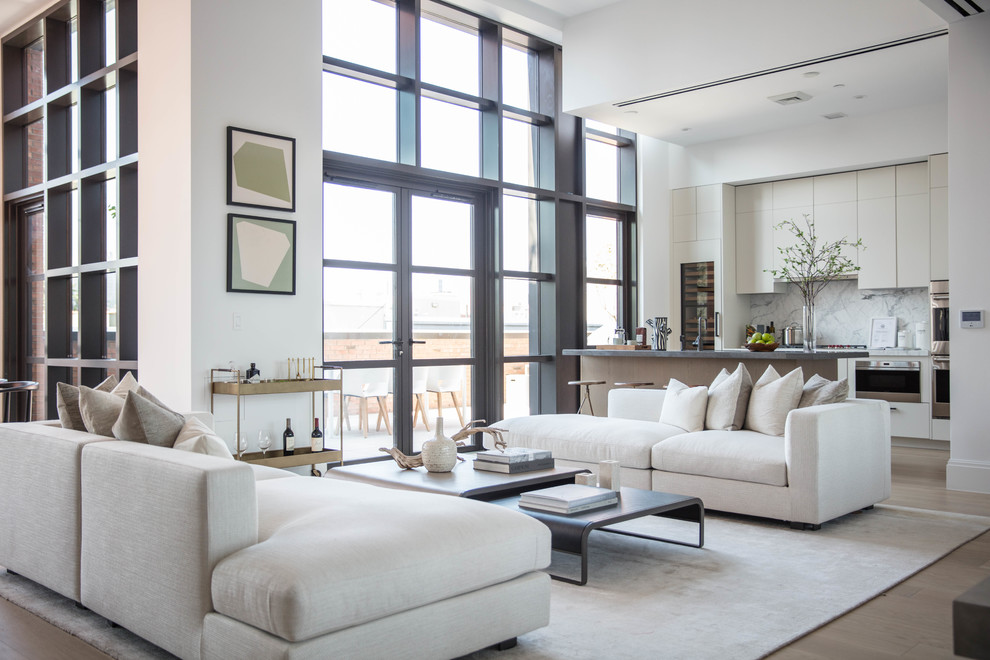 This is an example of a contemporary open concept living room in New York with white walls, light hardwood floors and a home bar.