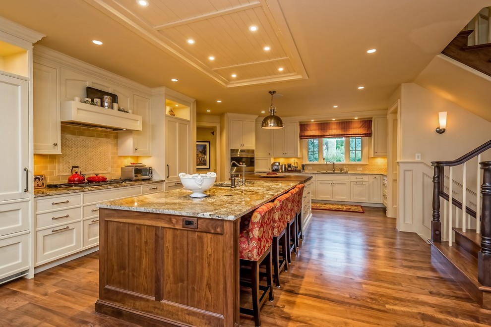 This is an example of a mid-sized traditional galley open plan kitchen in Denver with an undermount sink, shaker cabinets, white cabinets, granite benchtops, beige splashback, ceramic splashback, stainless steel appliances, dark hardwood floors, with island and brown floor.