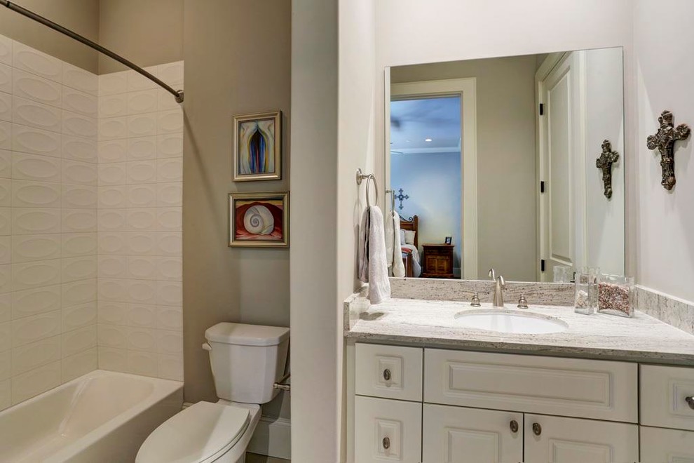 Photo of a mid-sized transitional kids bathroom in Houston with shaker cabinets, white cabinets, a two-piece toilet, gray tile, stone tile, an undermount sink, granite benchtops, grey walls, porcelain floors, an alcove tub and a shower/bathtub combo.
