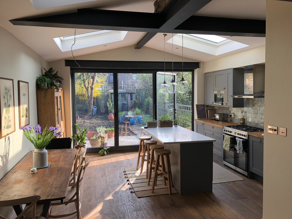 Photo of a mid-sized contemporary single-wall open plan kitchen in London with a farmhouse sink, shaker cabinets, grey cabinets, wood benchtops, grey splashback, porcelain splashback, stainless steel appliances, dark hardwood floors, with island, brown floor and yellow benchtop.