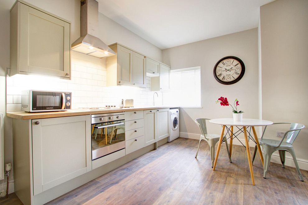Photo of a contemporary single-wall eat-in kitchen in London with shaker cabinets, white cabinets, wood benchtops, white splashback, subway tile splashback, stainless steel appliances, light hardwood floors and no island.
