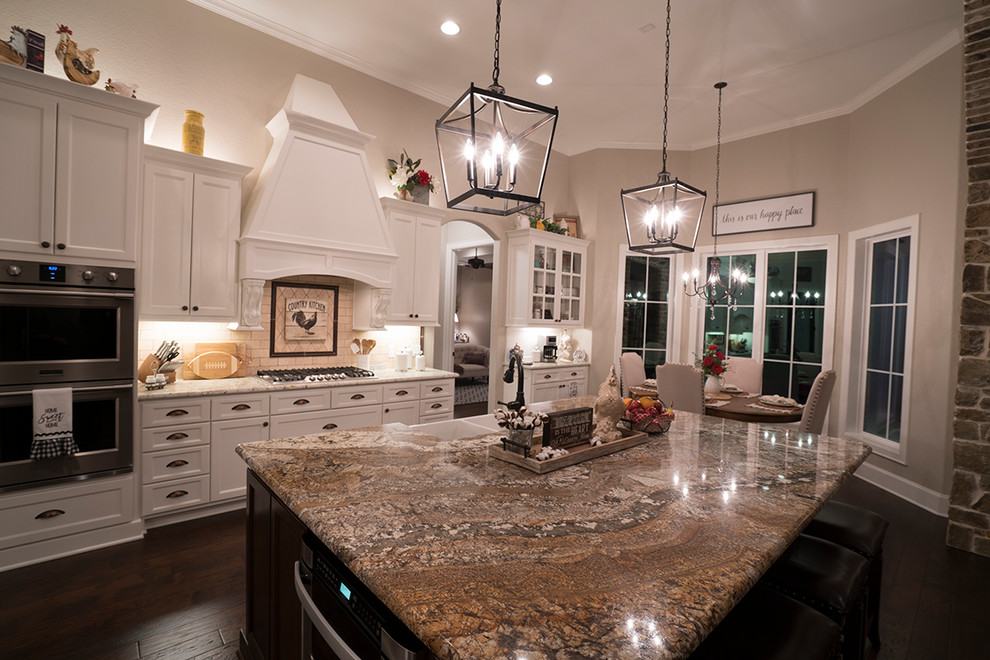 Design ideas for a mid-sized traditional l-shaped eat-in kitchen in Austin with a farmhouse sink, shaker cabinets, white cabinets, granite benchtops, beige splashback, stone tile splashback, stainless steel appliances, dark hardwood floors, with island and brown floor.