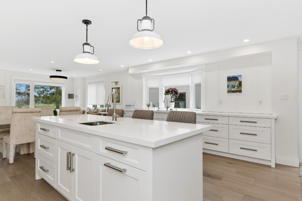 Inspiration for a large transitional u-shaped light wood floor and brown floor eat-in kitchen remodel in Toronto with an undermount sink, recessed-panel cabinets, white cabinets, quartz countertops, white backsplash, quartz backsplash, stainless steel appliances, an island and white countertops