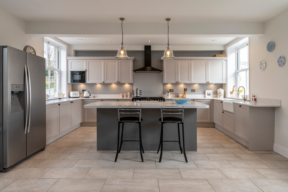 This is an example of a mid-sized transitional u-shaped eat-in kitchen in Cheshire with a farmhouse sink, quartzite benchtops, ceramic floors, with island, grey floor, grey benchtop, recessed-panel cabinets, grey cabinets and stainless steel appliances.