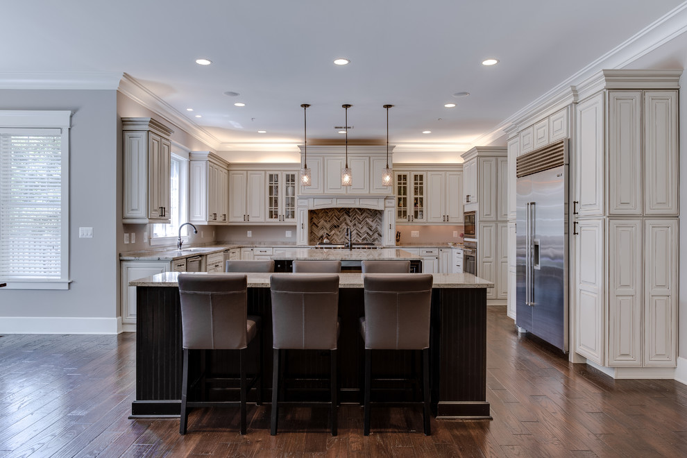 Large u-shaped medium tone wood floor eat-in kitchen photo in DC Metro with a drop-in sink, raised-panel cabinets, distressed cabinets, granite countertops, beige backsplash, glass tile backsplash, stainless steel appliances and two islands