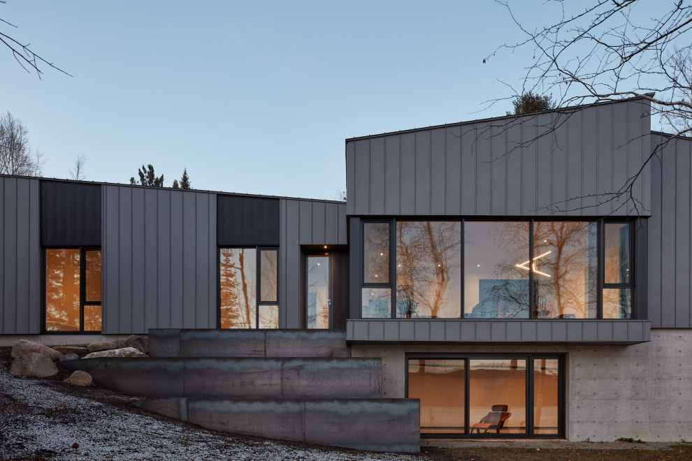 This is an example of a large contemporary two-storey grey house exterior in Montreal with metal siding, a clipped gable roof, a metal roof, a grey roof and clapboard siding.