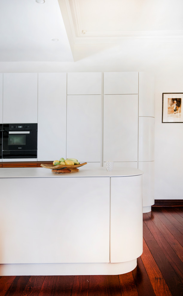 Idéer för att renovera ett funkis vit vitt kök och matrum, med vita skåp, stänkskydd i porslinskakel, mörkt trägolv, en köksö och brunt golv