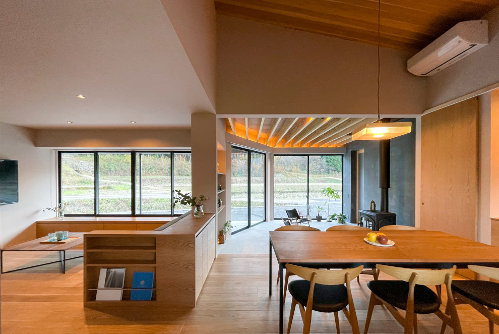 Cette photo montre une salle à manger ouverte sur le salon moderne avec un mur blanc, un sol en bois brun, un poêle à bois, un manteau de cheminée en béton, un sol marron, un plafond en bois et du papier peint.