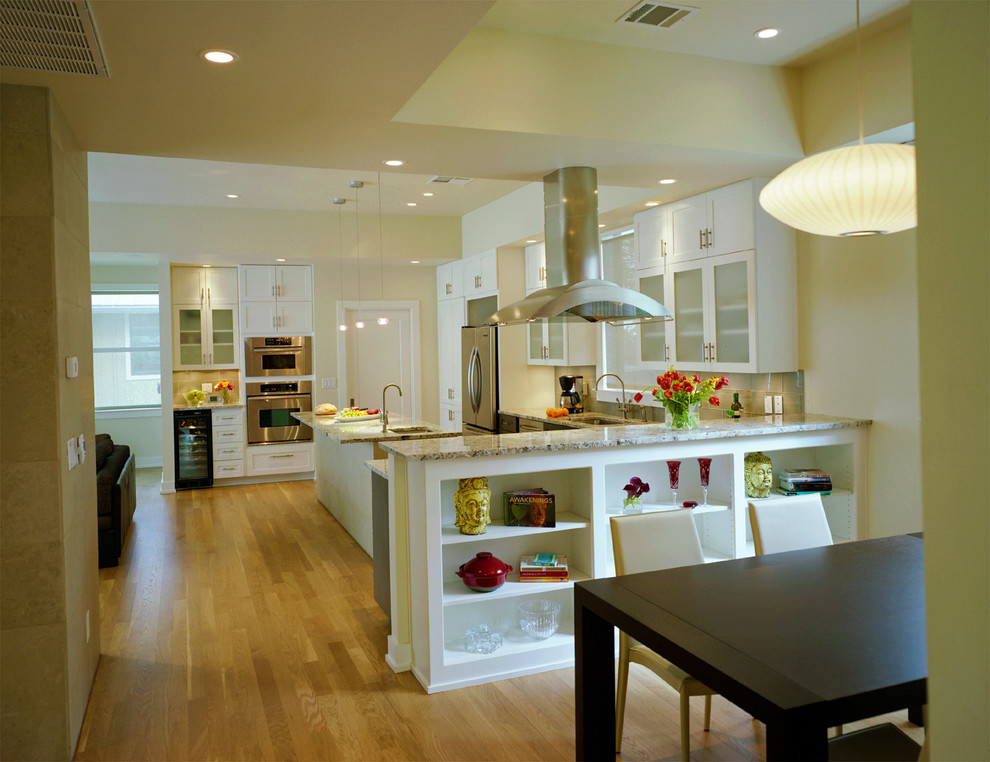 Photo of a transitional l-shaped open plan kitchen in Austin with stainless steel appliances, glass-front cabinets, white cabinets and granite benchtops.
