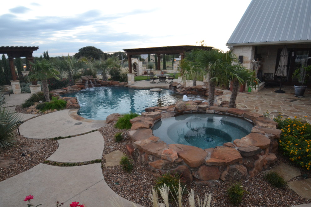 This is an example of a mid-sized custom-shaped natural pool in Dallas with a water feature and concrete pavers.