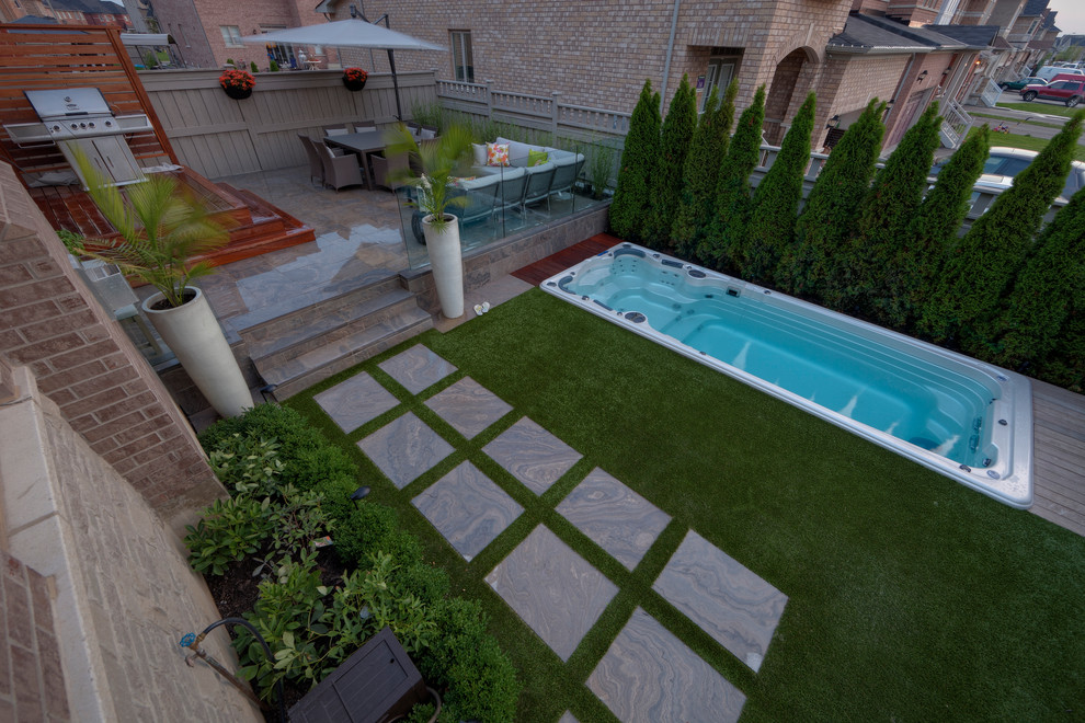 Small modern backyard rectangular lap pool in Toronto with natural stone pavers.