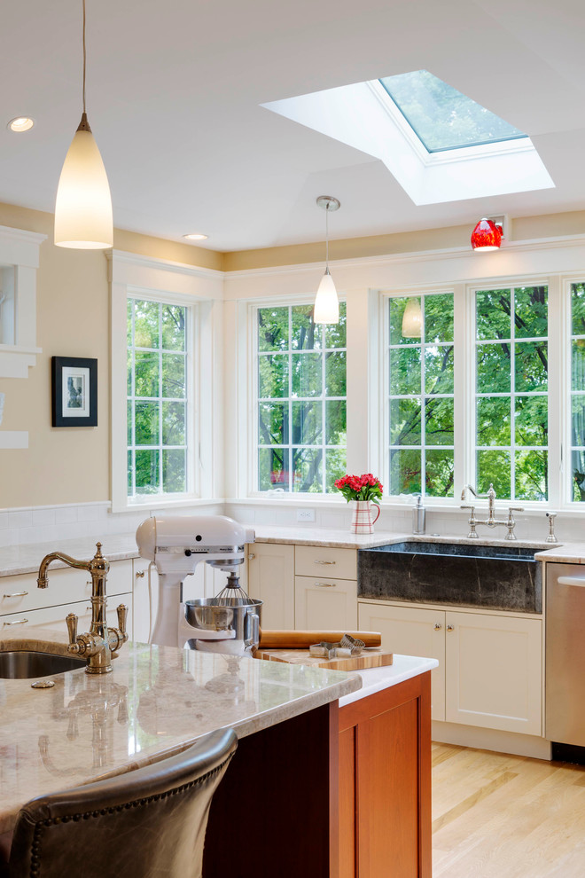 Large transitional l-shaped light wood floor kitchen photo in Boston with a farmhouse sink, recessed-panel cabinets, white cabinets, quartz countertops, white backsplash, subway tile backsplash, stainless steel appliances and an island