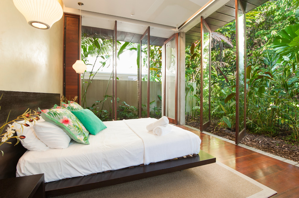 Design ideas for an expansive tropical master bedroom in Cairns with yellow walls and dark hardwood floors.