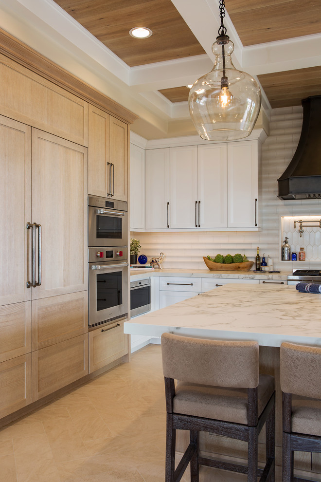 Photo of a large transitional l-shaped open plan kitchen in Denver with a farmhouse sink, recessed-panel cabinets, white cabinets, quartz benchtops, white splashback, ceramic splashback, panelled appliances, limestone floors, with island, beige floor and white benchtop.