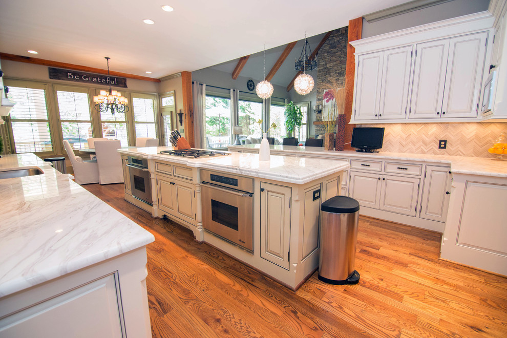 Inspiration for a mid-sized traditional u-shaped eat-in kitchen in Atlanta with a drop-in sink, recessed-panel cabinets, white cabinets, marble benchtops, white splashback, stone tile splashback, stainless steel appliances, medium hardwood floors and with island.